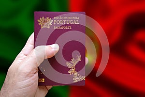 Man`s hand holding Portuguese passport with defocused Portuguese flag in the background. Written in Portuguese: European Union