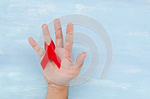 Man`s hand holding red AIDS ribbon. Aids Awareness campaign on 1st December day on blue wall background