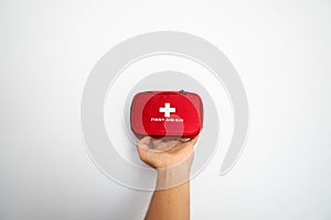 Man`s hand holding a red first-aid kit with a white wall on background.