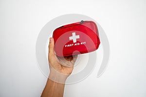 Man`s hand holding a red first-aid kit with a white wall on background.