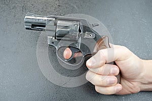 Man`s hand holding a revolver against a gray background, finger on the trigger