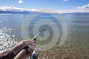 Man`s hand is holding a rishing rod with unfocused lake