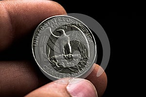 Man's hand holding a silver American coin, close-up of a quarter dollar coin isolated over black. Bag, dollars