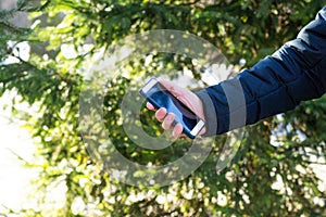 Man& x27;s hand is holding smartphone in hand on tree background outdoors. Concept of communication, call, messaging business