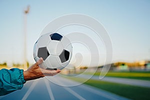 Man`s hand holding soccer ball on running track