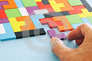 Man`s hand holding a square tangram puzzle, over wooden table.