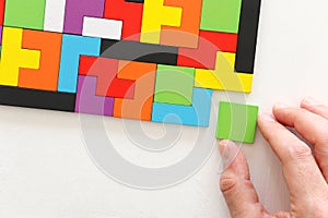 Man`s hand holding a square tangram puzzle, over wooden table