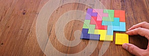 Man`s hand holding a square tangram puzzle, over wooden table