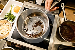 Man's hand holding steel stewpan standing on kitchen scales. Chief cooking spices in stewpan.