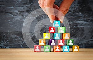 man& x27;s hand holding a top of wooden blocks pyramid with people icons over wooden table