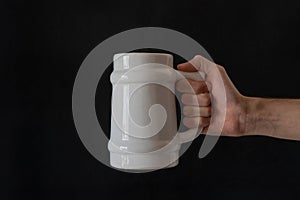 Man's hand holding a white ceramic beer mug.