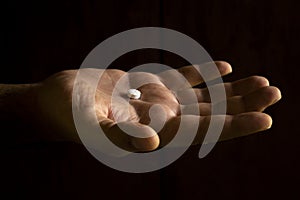 A man`s hand holding a white pill on a black background. Free space to write. Drug for legal use