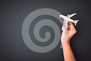 Man`s hand holding white toy airplane model over black color wall background with copy space, concept of travel