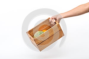 A man`s hand holding a wooden box containing melons and oranges.