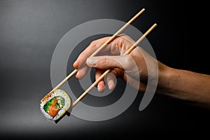 Man& x27;s hand holding wooden chopsticks with one piece of Philadelphia sushi roll