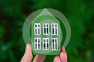 Man`s hand holding wooden house on green background. Sweet home and family concept