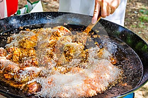 Man`s hand holding wooden turner, mixing uncooked rice with fried chicken meat tomato sauce spices. Preparing paella or jambalaya