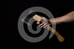 A man`s hand holds an ax on a black background.
