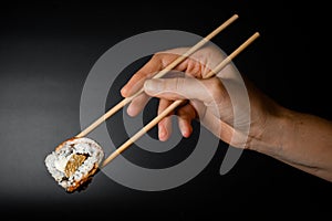 Man& x27;s hand holds bamboo chopsticks with Philadelphia sushi roll with smoked eel, salmon and cream cheese