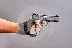 A man& x27;s hand holds a black pistol in his hand on a gray background