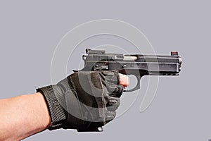 A man& x27;s hand holds a black pistol in his hand on a gray background