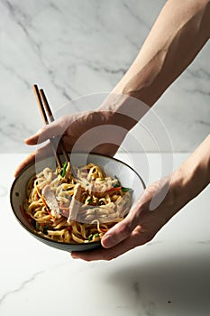 Man& x27;s hand holds a bowl with healthy Thai chicken noodle salad. Fresh and cold boiled rice noodles with chicken and