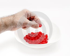 Man's hand holds a cherry over a white bowl with delicious red dried cherries. White background