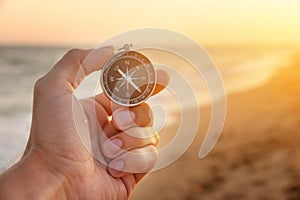 man& x27;s hand holds a compass on the beach. Hand with compass over sand by the sea, direction and adventure concept