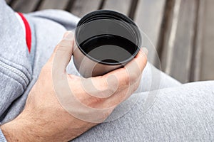 A man`s hand holds a Cup of tea or coffee from a thermos.