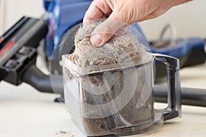 Man& x27;s hand holds dirt and dust out of the vacuum cleaner container and shows it close up