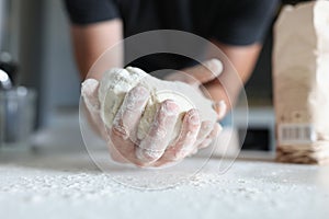 Man`s hand holds the dough over table where flour is scattered.