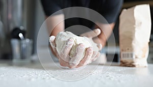 Man& x27;s hand holds the dough over table where flour is scattered.