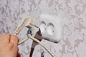 A man\'s hand holds an electric plug and a damaged cable. The danger of an electric shock