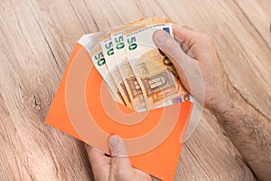Man`s hand holds an envelope and removes from it Euro banknotes with denominations of 50 Euro.