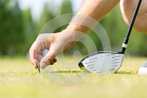 Man& x27;s hand holds a golf ball on a stand in the green grass against the background of the sky with clouds