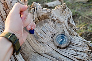 Man`s hand holds a knife for survival stuck in an old, dried tree, next to a compass.