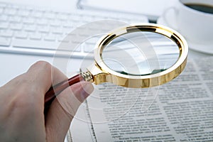 Man`s hand holds a magnifying glass over a newspaper
