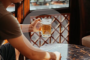 Man`s hand holds a mug of beer. Mug in the center of the photo. A pint of light beer