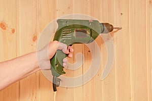 Man`s hand holds an old electric drill and drills a wooden wall