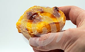 A man& x27;s hand holds one Portuguese Pastel de Nata pie with custard and cinnamon sticks on a white background. Pastel
