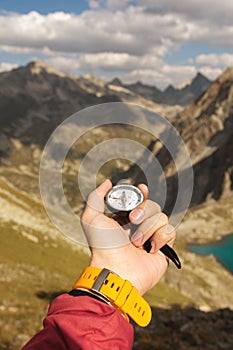 A man`s hand holds a pocket magnetic compass for navigation against the backdrop of a rocky slope and a mountain. The