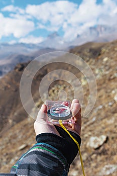 A man`s hand holds a pocket magnetic compass for navigation against the background of a rocky slope and epic rocks under