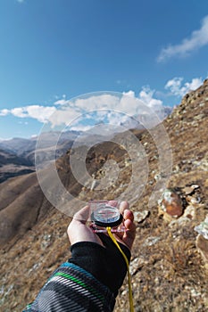 A man`s hand holds a pocket magnetic compass for navigation against the background of a rocky slope and epic rocks under