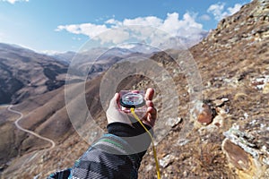 A man`s hand holds a pocket magnetic compass for navigation against the background of a rocky slope and epic rocks under