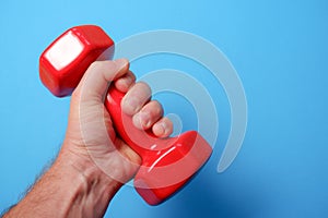A man's hand holds a red plastic dumbbell on a blue background. Fitness concept