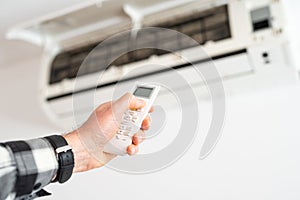 A man& x27;s hand holds a remote control from an air conditioner with a temperature on the screen of 21