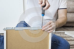 The man`s hand holds the screwdriver and screws the screw that secures the drawer guide.