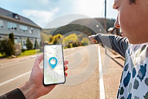 A man`s hand holds a smartphone with an online map, and a teenager points the way with his hand. In the background is a city