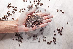 Man`s hand holds some coffee beans in his palm on a marble table with copy space for your text