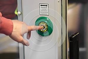 Man& x27;s hand index finger presses the door control green button to open doors in a modern electric train or subway car